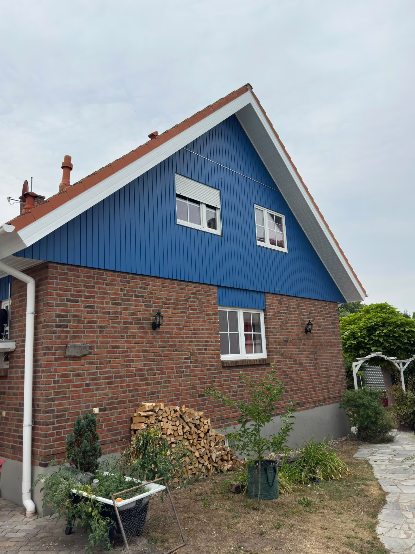 Wohnhaus mit blauer Holzfassade am Giebel und rotem Klinkermauerwerk
